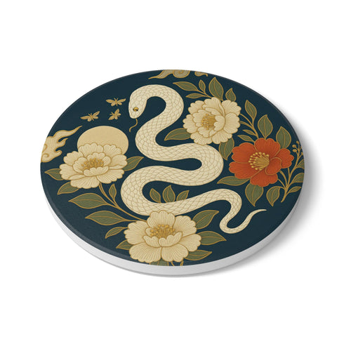 Round ceramic coaster with a chinoiserie-inspired design featuring a white snake among golden peonies, butterflies, and a glowing moon on a dark green background. Surrounded by floral and botanical accents with a soft vintage aesthetic. The coaster has a cork back and measures about 4 inches in diameter. Ideal for mugs, teacups, or wine glasses, this decorative piece suits witchy, victorian, and chinoiserie-inspired decor.